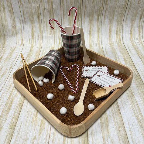 "Keep warm and toasty this winter! Your little learner will love the aspect of dramatic play that comes with this hot cocoa sensory bin! This set features 12 recipe cards for your child to use to create their wintery drink, while practicing skills like number recognition, counting and direction-following, as well as fine motor skills such as scooping, dumping, and using tongs. What's included? -5c brown rice -2 cups (paper, to-go style) -2 wooden spoons -6 candy canes -10 pom pom \"marshmallows\ Hot Cocoa Sensory Bin, Sensory Bin Winter, Winter Sensory Bin, Winter Sensory, Wooden Scoop, Number Recognition, Plastic Bins, Loose Parts, Sensory Bin