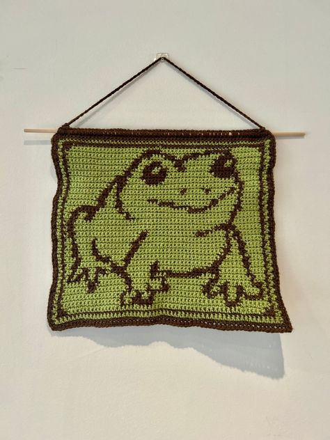 🐸Make your own cute frog crochet tapestry!🐸 📏 This tapestry is approximately 30cm x 26cm in size, measured from the bottom of the dowel rod 📏 ✍🏼This pattern includes instructions that have been written out in 3 different ways 1. Stitch Fiddle Graph  2. Colour Block Instructions  3. Written Instructions  🧶Materials needed:🧶 - 4mm crochet hook (can use other sizes at your own discretion) - Green DK wool  - Brown DK wool - Dowel rod - Scissors - Darning needle 🌱Stitches used in pattern:🌱 - Frog Crochet Blanket Pattern, Frog Tapestry Crochet, Funny Tapestry Crochet, Small Tapestry Crochet Pattern, Crochet Tapestry Pattern Free, Frog Tapestry, Crochet Tapestries, Creepy Crochet, Stitch Fiddle