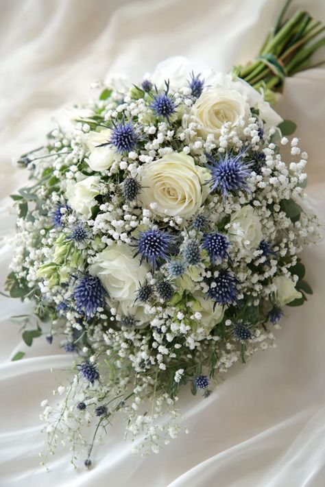 A bouquet of white roses, babys breath, and blue thistle flowers, arranged elegantly on a soft, white fabric background. White Fabric Background, Bouquet With White Roses, Bouquet Of White Roses, Blue And White Roses, Thistle Wedding, White Rose Wedding Bouquet, Blue Carnations, Blue Thistle, White Rose Bouquet