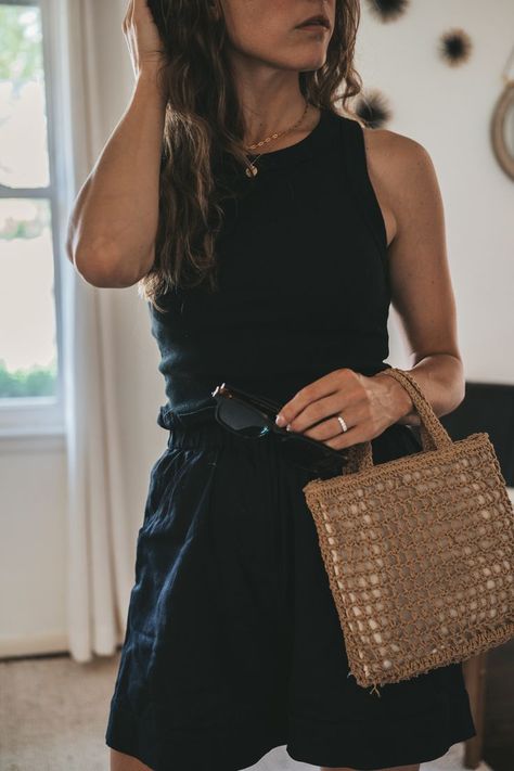 ashley wearing a black ribbed tank, black paperbag shorts, black strappy sandals, and a woven bag with tortoise shell sunglasses; a black mid century modern side chair in the background Black Shorts Outfit 2023, Black Belted Shorts Outfit, Black Tank Outfit Summer, Black Ribbed Tank Top Outfit, Minimal Outfits Summer, Edgy Classic Summer Outfits, Minimal Chic Style Outfits Summer, Black Shirt Black Shorts Outfit, Styling Black Linen Shorts