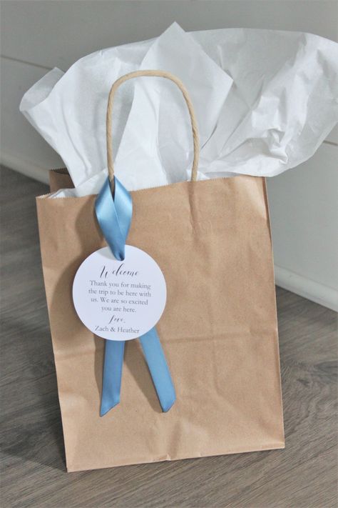 "A gorgeous, yet simple way to welcome your out-of-town wedding guests when they get to the hotel for your big day! Shown with smoke blue ribbon DETAILS: Choose from several options to suit your needs FULL SET, ASSEMBLED, INCLUDES: * Kraft bag with twine handles * Bag measures 10.5\" tall x 8\" wide x 4.75\" deep * Includes tag personalized with your initials and wedding date- measures 3\"x3\" * Includes ribbon * Includes one sheet of large white tissue paper * Arrives assembled and ready for yo Wedding Guest Care Package Welcome Bags, Wedding Favor Bags For Guests, Gift Bags For Wedding Guests At Hotel, Welcome Gifts For Guests Wedding, Out Of Town Wedding Guest Bags, Hotel Welcome Bags Wedding Goodies, Wedding Hotel Welcome Bags Ideas, Diy Wedding Welcome Bags, Wedding Welcome Bag Ideas