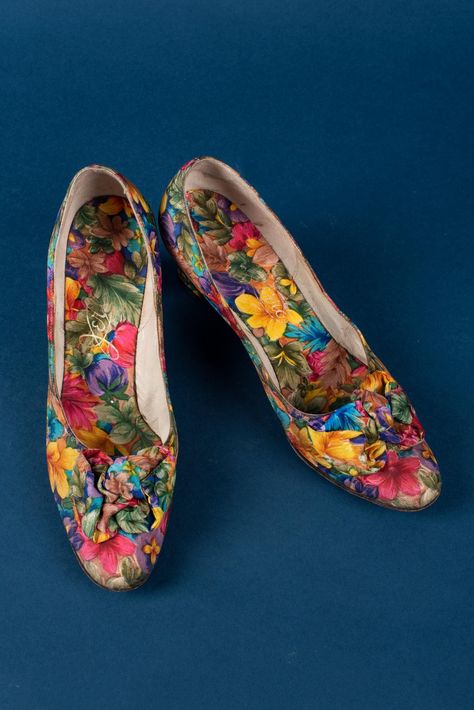 Pumps of multi-colored floral fabric in red, purple, yellow, and green print. Round toe box with large three-dimensional flowers of self, round moderate throat. 1-1/2" heel covered in self, lined in self. Size 5M    Measurements:  L: 22.5 cm.  W: 7 cm.  H: 11.5 cm.  Heel: 6 cm, 2.5 inches    Markings L&R: "Jerro" Oklahoma History, Texas Fashion, Floral Pumps, University Of North Texas, Red River, Yellow And Green, Green Print, Historical Fashion, Floral Fabric