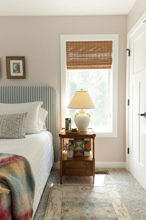 Vintage nightstands with a striped DIY upholstered headboard. White bedding and a pattern lumbar pillow. Woven rattan shades and warm wood nighstands. Designer bedroom with carpet. Beachy Nursery, Beach Cottage Bedroom, Diy Upholstered Headboard, Bed Board, South Haven Michigan, Beachy Bedroom, Bedroom Styling, South Haven, Rattan Shades