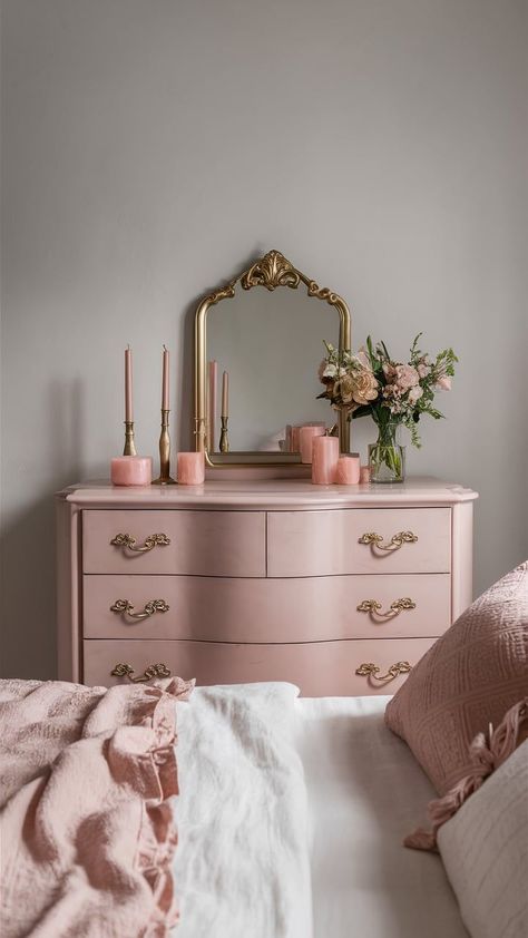 A soft blush pink dresser with gold handles, set against a light gray wall, adorned with delicate decor items like a gold-framed mirror, candles, and fresh flowers. Baby Pink Dresser, Vintage Pink And Gold Bedroom, Pink And Gold Dressing Room, Pink Academia Room, Pink Vintage Aesthetic Room, Vintage Pink Bedroom Ideas, Blush Pink And Gold Bedroom, Blush Pink Dresser, Dresser Decor Ideas