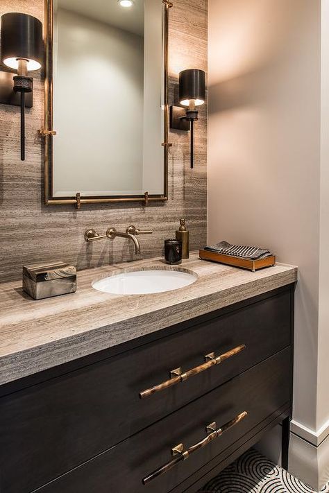 Black sconces flank a gold and black mirror hung from a brown stone backsplash over a brushed gold wall faucet fixed over a dark brown footed washstand. Bathroom Decor Black, Bathroom Brown, Brown Sofa Living Room, Brown Bathroom Ideas, Cream Bathroom, Brown Living Room Decor, Brown Bathroom Decor, Black Sconces, Dark Bathrooms