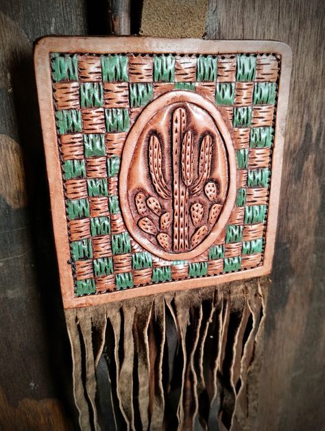 Tooled leather hanging piece that features a Cactus design in the center and a green checkered background. On the back is a cutout cactus.  Hangs from a piece of Leather cord.  Light leather fringe hangs beneath.  Measures 8.75 inches from the top of the tooled piece to the bottom of the fringe and 3 7/8 inches wide.  Add accent to a wall or hang from your rearview mirror in your vehicle. Green Checkered Background, Leather Wall Art, Cactus Western, Checkered Background, Leather Patterns, Western Home, Green Checkered, Cord Light, Leather Wall