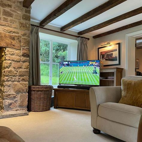 This living room is given a rustic lodge look with a darkly stained exposed beam ceiling running towards the natural stone fireplace. Coordinate a neutral sofa and dark wood furniture to complete this cozy look. Beamed Living Room, Beams On Flat Ceiling Living Room, Dark Wood Beams On Ceiling, Dark Beams Living Room, Exposed Beams Ceiling Living Room, Wood Beam Ceiling Living Room, Low Living Room, Entrance Ceiling, Natural Stone Fireplace