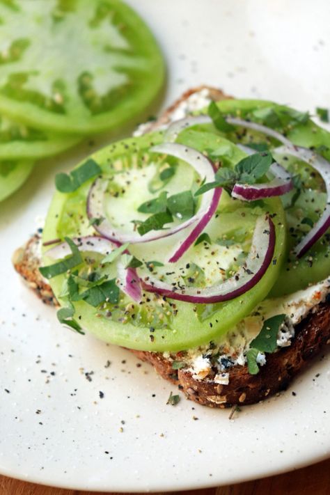 Green tomato toast with goat cheese, red onion and fresh herbs on a white plate Heirloom Tomatoes Toast, Green Tomato Breakfast, Red Tomato Recipes, Garden Fresh Tomato Recipes, Raw Tomato Recipes, Tomato Recipes Dinner, Green Tomatoes Recipes, Green Tomato Soup, Cheese And Tomato Sandwich