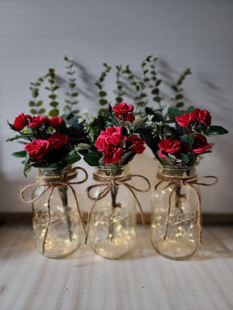 "These beautiful faux mini-rose quart size mason jar centerpieces are a Glassy Gal original design. Each centerpiece includes one set of warm white LED fairy lights, a jute bow, a deluxe faux greenery arrangement with mini roses. You can choose your mini rose color at checkout. These centerpieces are very popular for weddings, baby showers, parties, corporate events, holiday events, and any other event that requires table centerpieces. They also look great in any room of your house or office. To see other lighted jar options and all of my other listings, please view my shop: https://www.etsy.com/shop/GlassyGalDecor Each jar set includes: (1) clear quart size mason jar (1) set of LED fairy lights (1) deluxe faux greenery arrangement (includes 3 tall eucalyptus stems, 2 short silver dollar Table Decoration With Lights, Restaurant Centerpieces Simple, Small Elegant Centerpieces, Rose Themed Birthday Party Decorations, Black And Red Centerpieces, Valentine Table Centerpieces, Red And Gold Centerpieces, Valentines Table Centerpieces, Valentines Centerpiece Ideas