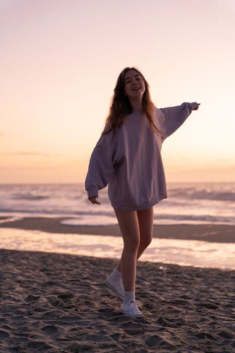 girl in oversized lilac sweatshirt and converse walking on the beach at sunrise smiling with and arm in the air Morning Beach Photoshoot, Morning Beach Pictures Poses, Early Morning Beach Photoshoot, Lowkey Beach Poses, Windy Beach Pictures, Sunrise Shoot, Morning Beach Walk, Morning Beach, Almond Eyes