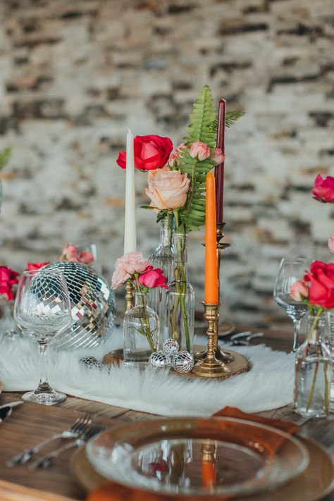 We had so much fun styling this boho disco themed shoot! We used vintage elements in combination with classic boho decor to make a super fun and unique table. These long farm tables are great for styling unique centerpieces. For ours, we used a combination of vintage candlestick holders, bud vases filled with assorted pink flowers, shiny disco balls, and went with a fun fur throw as a table runner. Sparkly and metallic gold chargers looked just right with a warm brown napkin. Shot by @kaboovang Disco Ball Wedding Tables, Boho Disco Centerpieces, Fun Flower Vases, Pink Bud Vases Wedding, Centerpieces With Disco Balls, Disco Centerpieces Wedding, Disco Wedding Flowers, Disco Wedding Table Setting, Disco Ball Wedding Table Decor