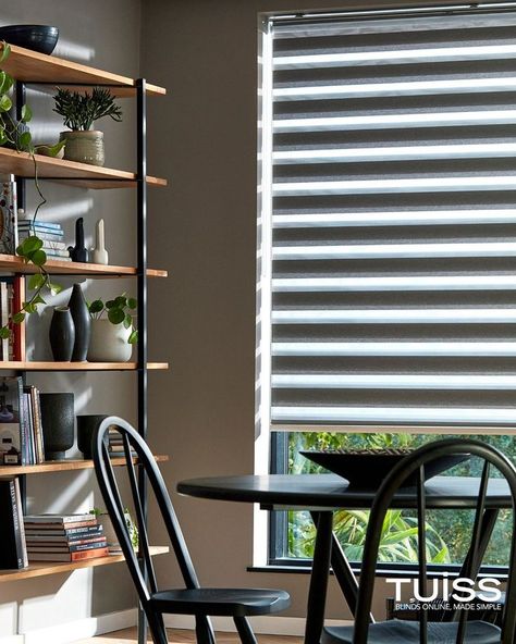 A stylish living room featuring a set of zebra blinds on a large window, allowing natural light to filter through. The room is decorated with a modern black dining table and matching chairs, a wooden shelving unit with various plants, books, and decorative items, creating a cosy and contemporary atmosphere. Black Dining Set, Zebra Blinds, Modern Minimalist Living Room, Black Dining, Home Design Living Room, The Perfect Day, Take Two, Minimalist Living, Light Control