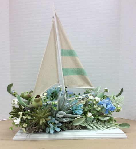 Sailboat floral arrangement I made. Glued styrofoam to painted wood plaque.  Foam was in a wedge shape so boat would tilt up when glued to foam. Added Spanish moss, succulents and other florals. Seaside Floral Arrangements, Lighthouse Floral Arrangements, Boat Flower Arrangement, Coastal Flower Arrangements, Coastal Floral Arrangements, Beach Flower Arrangements, Beach Arrangements, Nautical Centerpiece, Contemporary Flower Arrangements