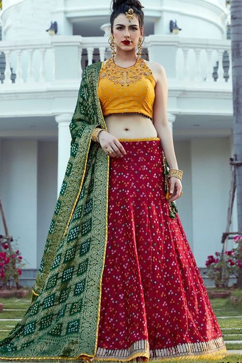 Look youthful in this colorful designer lehenga choli set featuring a red bandhani lehenga and contrasting yellow halter neck choli printed in white bandhani style motifs and worked in glorious resham & zari embroidery in a look of young grandeur! This lehenga choli set comes with can can & is accompanied with contrasting green bandhani dupatta. Green Bandhani Dupatta Lehenga, Green Bandhani Saree Blouse Design, Red Bandhani Lehenga, Green Bandhani Dupatta, Bandhani Lehenga, Dress Designs For Girls, Red Lehenga Choli, Bandhani Dupatta, Designer Bridal Lehenga Choli