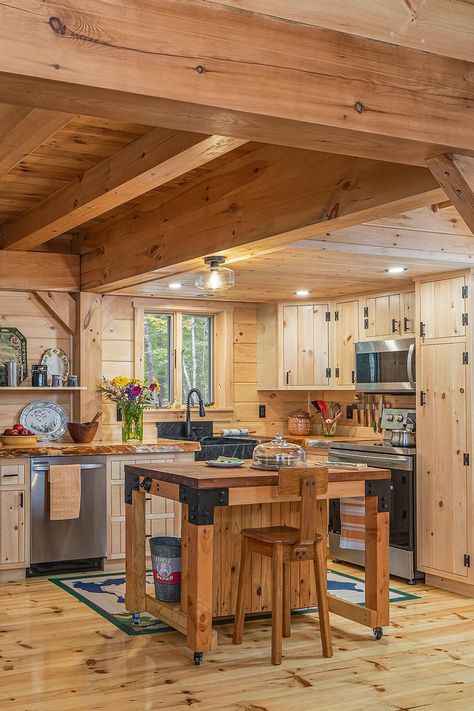 Spacious and cozy at once, the open kitchen boasts a pantry, movable island (handmade by homeowner Wayne from reclaimed wood and steel brackets), knotty pine tongue-and-groove cabinetry, locally sourced pine floors, a soapstone sink and stainless-steel appliances. Photography by Mark Sorenson. Post And Beam Homes Interior, Log Home Kitchen Ideas, Knotty Pine Living Room, Movable Island, Soapstone Sink, Knotty Pine Kitchen, Log Cabin Flooring, Timber Frame Kitchen, Chalet Kitchen