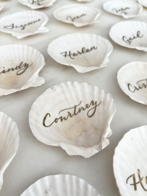 Scallop shells featuring gold calligraphy by Nob Hill Jane are a unique place card idea for your coastal or beach themed wedding. Beach Theme Place Settings, Beach Wedding Table Assignments, Seashell Place Cards, Shell Place Cards Wedding, Seashell Name Cards, Coastal Place Settings, Shell Name Cards Wedding, Coastal Themed Wedding, Oyster Shell Seating Chart