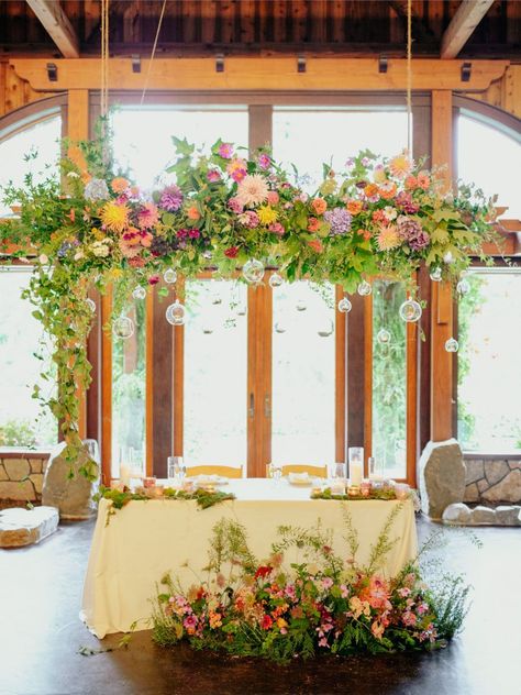 Bright Hanging Floral Installation, Wild Flower Floor Arrangement, Flower Installation Hanging, Freeform Flower Arrangements, Wildflower Hanging Installation, Wildflower Bride And Groom Table, Wildflower Top Table, Hanging Flowers Above Table, Wild Flower Sweetheart Table