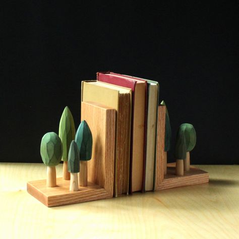 "These hand carved book ends could be the perfect gift for a loved one who is happiest when they are surrounded by trees!  I have carved fragrant cedar wood into these little stands of trees which I then stain in a variety of shades of green before affixing them to the sturdy yet satiny smooth white oak base.  I designed this set to sit on a shelf or mantel and corral books all while looking beautiful.  Each has been built with discreet joinery to last for ages.  A real heirloom quality piece th Book Stand Ideas, Bookends Ideas, Book Stand Design, Bookends Wood, Carved Tree, Scrap Wood Crafts, Wood Bookends, Wooden Bookends, Gift For Gardener