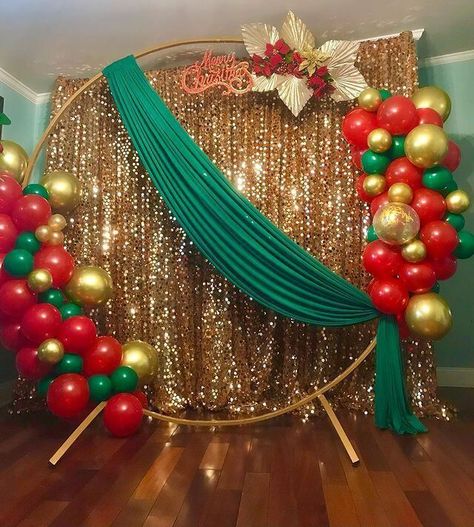 Set up a sparkling backdrop for your Christmas party using attractive decor elements. Cover the backdrop stand with shimmery gold sequin curtains for an enticing allure. Place a gold round arch at the front and arrange red, gold, and green balloons on it to impart a peppy appeal to your party decor. Also, stylishly drape green fabric and arrange red flowers along with gold leaves on the stand oozing oodles of glimmer and shimmer. Green And Gold Christmas Decor, Ideas Christmas Decoration, Green And Gold Christmas, Decoration Ideas Christmas, Christmas Party Backdrop, Sequin Curtains, Gold Christmas Decor, Christmas Balloon Decorations, Birthday Decorations At Home