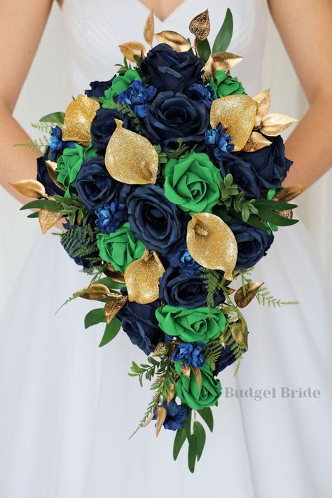 This lovely assortment of navy blue and emerald green roses, blue delphininium, and luxurious greenery is bound to turn heads on your wedding day. This lovely cascading brides’ bouquet from the Marilee collection is an absolutely breathtaking arrangement for any bride to be, in any season. Gold glitter calla lilies and gold leaves complete the look and add a delicate realism to this beautiful bouquet. This bouquet is 10” wide, 18” long, and is crafted by our in-house florists without using a foa Navy Blue And Emerald Green Wedding Bouquet, Emerald Green And Royal Blue Wedding, Navy Blue And Emerald Green Wedding, Blue And Emerald Green Wedding, Emerald Green And Navy Blue Wedding, Emerald And Navy Wedding, Blue And Green Wedding Theme, Navy Blue And Emerald Green, Blue And Green Wedding