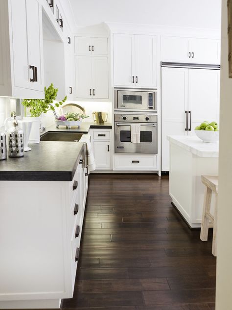 Lovely kitchen with crisp white shaker cabinets paired with soapstone countertops and white marble backsplash. Black Counter White Island, White Kitchen With Soapstone Countertops, White Kitchen Cabinets With Black Soapstone Counters, White Kitchen Soapstone Countertops, White Cabinet Soapstone Countertop, White Kitchen With Dark Floors, Soapstone Counter With Marble Backsplash, Kitchen Dark Floors, White Kitchen Dark Floors