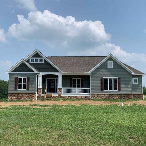 This cottage-style ranch home features a harmonious blend of design elements. The Fairfax brown front door, set against the Aspen-colored siding, creates a rich contrast.  The Provia shake siding in Timberline, used on the front gables over the porch and bedroom 2, adds texture and warmth. The Dutch Quality Autumn blend limestone, which clads the watertable and porch post piers, introduces natural stone elements that harmonize with the earthy tones, creating a cozy and inviting exterior. Cedar Shake Siding Accent, Brown Front Door, Brown Front Doors, Cedar Shake Siding, Shake Siding, Floor Plans Ranch, Unique Floor Plans, Cedar Shakes, Ranch Exterior