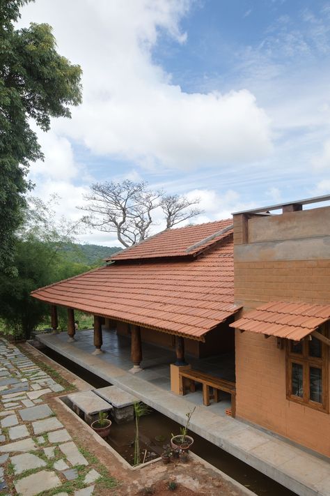 Ra Maram located in Manchi reserve forest has been designed to align with the principles of cradle to grave concept, minimising the carbon footprint and embodied energy of the construction. The walls are of stabilised mud blocks with the foundation and certain feature walls, being of local Sadarhalli stone, sourced and sized from within the site. The wood was re-purposed from an abandoned factory near-by. #CSEB #Mangalore tile roof #Earth architecture Kerala Roof Tile Design, Manglore Tiles Roof, Mud House Indian Modern, Mud Block Houses, Mud House Exterior, Vernacular Architecture Indian Concept, Cseb Construction, Roof Ideas Architecture Design, Mud House Design Ideas