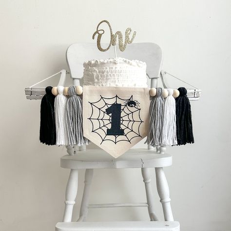 Celebrate your little one's 1st birthday with our spooky spider Halloween birthday party decorations! Our spider web themed high chair banner adds a magical touch to the celebration. Designed for a 1st birthday, this spooky Halloween decor will make your event truly unforgettable. Whether you're planning a bewitching bash or a cozy gathering, our decorations will create a charmingly eerie atmosphere that guests will love.  The canvas center flag has a spider web with a cute spider and a black number 1 in the middle. It has one each of gray, white and black tassels on either side.  You have the option to add the ONE gold glitter cake topper.  Don't forget too add a matching balloon tower, or a spooky spider balloon from our sister store! Balloon tower: https://www.etsy.com/listing/178296852 Spooky One Highchair Banner, Goth First Birthday, Halloween One Year Birthday, Halloween First Birthday Boy, Halloween 1st Birthday Party, Spider Balloon, Halloween Birthday Party Decorations, Halloween First Birthday, Halloween 1st Birthdays