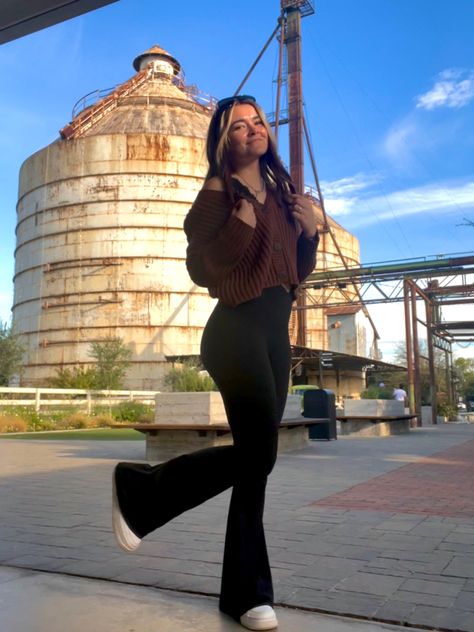 Girl wears a brown off the shoulder top from American Eagle paired with black crossover flared leggings from Aerie. Also wearing white Air Force 1’s. Posing in front of the Silo’s at Magnolia Market in Waco, Texas. American Eagle Flare Leggings, Flared Crossover Leggings Outfit, Brown Flare Leggings Outfit Winter, Aerie Crossover Flare Leggings Outfit, Tops To Wear With Flare Leggings, Brown Flair Legging Outfit, Outfits With Brown Flare Leggings, Black Flare Leggings Outfit Fall, Crossover Leggings Outfit