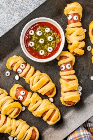 Mummy Hot Dogs: These baked hot dogs are wrapped in crescent dough strips to make an easy, tasty Halloween party food! Serve these mummy hot dogs with a spooky monster eye dip to take them over the top! Crescent Wrapped Hot Dogs, Monster Dip, Mummy Hot Dogs Recipe, Halloween Mummy Hot Dogs, Mummy Hot Dogs, Baked Hot Dogs, Wrapped Hot Dogs, Easy Halloween Cookies, Halloween Party Appetizers