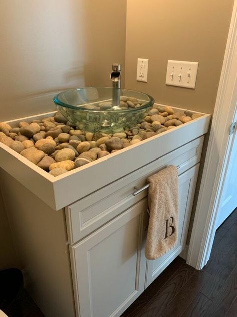 This is our natural river rock counter for our rustic , nature like half bath off our family room. We painted the room a warm Med brown . The cabinet is beige gray and we have a green wreath and two Paintings with green ferns in them.We made a wood tray 3 “ deep and painted it the exact color of the cabinet. We then installed the vessel sink and faucet. We added small multi colored pebbles and used a long stick to push them evenly under the sink so when you looked down into the sink th… Diy Bathroom Sink Vanity, Diy Vessel Sink, Bathroom Vanity With Vessel Sink, River Rock Bathroom, Rock Bathroom, Vanity With Vessel Sink, Diy River Rock, Sink Diy, Glass Kitchen Cabinet Doors