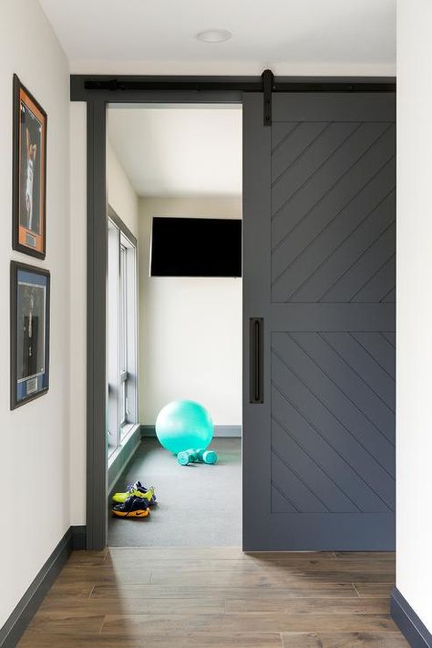 A dark gray plank barn door on rails is accented with a matte black handle and opens to a home gym boasting a flat panel television. Basement Home Gym, Basement Gym Ideas, Rustic Basement, Basement Gym, Home Gym Decor, Home Gym Design, Gym Decor, Sliding Doors Interior, Interior Barn Doors