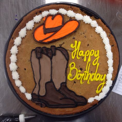 Western-themed cookie cake with brown cowboy boots and an orange cowboy hat. Cowboy 18th Birthday Party, Western Cookie Cake, Orange Cowboy Hat, Cowboy Hat Cake, Cowboy Boot Cake, Western Birthday Cakes, Cowboy Birthday Cakes, Cowboy Cookie, Cowgirl Cookies