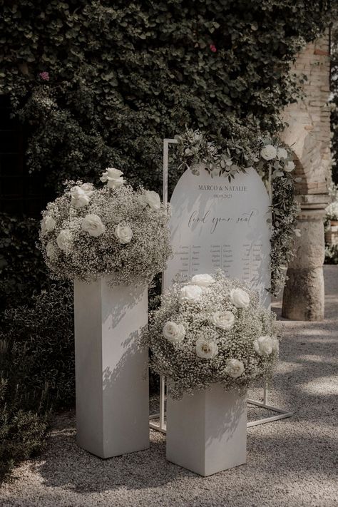 White roses and white gypsophila with white wedding table plan signage Wedding Decorations White Roses, White Flower Table Arrangements Wedding, White Flowers Decoration Wedding, White Rose Wedding Arrangements, Wedding Table Decorations White Flowers, White Rose Isle Wedding, White Black Sage Wedding, Diy White Flower Arrangements, Head Table Wedding Decorations Backdrops