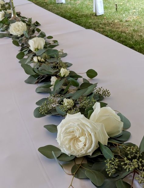 Simple garland of seeded eucalyptus and silver dollar eucalyptus with white roses and spray roses Roses And Eucalyptus Arrangement, White Roses Eucalyptus Centerpiece, Garland With Flowers, Masquerade Gala, White Rose Centerpieces, Simple Garland, Eucalyptus Centerpiece, Arbor Decor, Bridal Party Bouquets