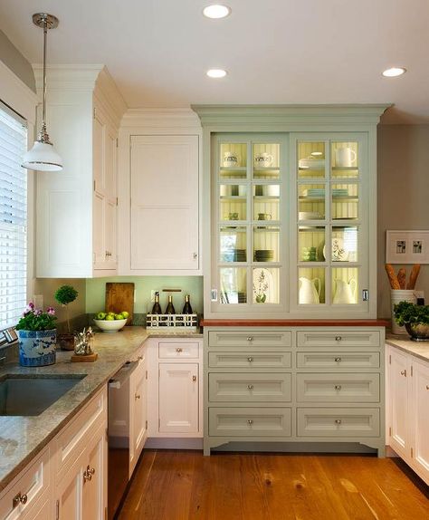 Country kitchen with integrated kitchen hutch with glass doors boasting beadboard backed lit shelves and brushed nickel hardware. The sage green hutch is next to white cabinetry accented with nickel cabinet pulls and natural stone counters alongside a painted backsplash. The kitchen features an undermount single basin sink illuminated by a white glass pendant with stainless steel dishwasher to the right over hardwood floors Built In Kitchen Hutch, Crown Point Cabinetry, Built In Hutch, Kitchen Hutch, Homemade Furniture, French Country Kitchens, French Country Kitchen, Transitional Kitchen, Kitchen Redo