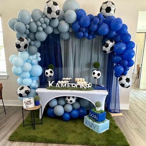 Welcome the little bundle of joy with a lively football-themed baby shower arrangement. Accentuate your tabletop with a white spandex cover paired with a royal blue runner. Also, display the confections using stylish cake and cupcake stands, along with lush greenery on the table. And don't forget the finishing touch – a vibrant green grass carpet rug laid under the table. Complete the look with blue & grey sheer drapes on a backdrop stand, adorned with blue and grey balloons for added charm. Green Grass Carpet, Drapes Backdrop, Grey Balloons, Stylish Cake, Party Decorations Table, Grass Carpet, White Spandex, Cake And Cupcake Stand, Cupcake Stands