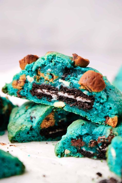 A close-up of a stack of vibrant blue Cookie Monster cookies, some broken to reveal a chocolate and cream center, located on a white surface. Small brown chunks are visible within the blue cookie dough. Cookie Monster Blue Cookies, Cookie Monster Cookies, Mexican Cocktails, Pie Dip, Homemade Recipes Dessert, Blue Cookies, Blue Food Coloring, Baking Party, Cheesecake Cookies