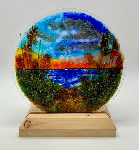 Introducing a captivating 9-inch Glass Fused Ocean Sunset Oasis. This circular masterpiece transports you to the serene beauty of an ocean sunset beach, capturing the warm hues of the sinking sun against the tranquil backdrop of sandy dunes and swaying beach grass. Meticulously crafted, this piece embodies the essence of coastal serenity, with each element - from the sun-kissed waves to the gentle rustle of beach grass - carefully fused into a harmonious composition. The circular design adds a sense of fluidity, enhancing the immersive experience of a peaceful seaside retreat. Please note that the display stand is not included, allowing you the freedom to choose one that perfectly complements your personal style. Whether adorning a tabletop or hung on a wall, let the Glass Fused Ocean Suns Fused Glass Sunset, Beach Grass, Glass Fusion, Christmas Lanterns, Ocean Sunset, Circular Design, Art Beach, Fused Glass Art, Glass Art Sculpture