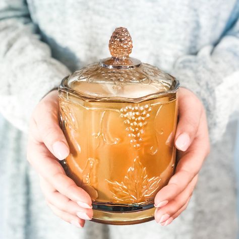 Immerse yourself in the charm of yesteryears with our Amber Carnival Glass Candy Jar, now repurposed with a customizable vintage candle. Choose your desired fragrance and let this hand-poured soy wax candle enhance your space with its enchanting vintage allure. The captivating jar features an iridescent amber shade and the classic Grape Harvest pattern. Originally introduced by Indiana Glass as a Candy Jar, it is steeped in history and nostalgia. It was not until years later that the medium and Unique Candle Containers, Pear Honey, Grape Harvest, Glass Candy Jars, Grape Harvesting, Teacup Candles, Vintage Candle, Hand Poured Soy Candles, Candle Inspiration