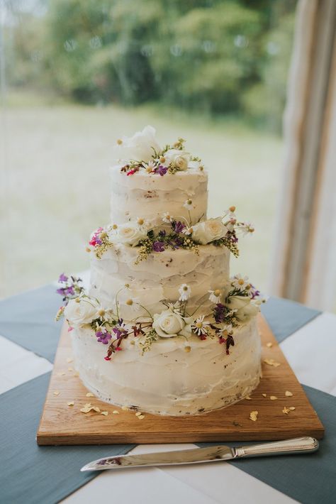 Three tier rustic white iced wedding cake with daisies and roses at marquee wedding Tiered Carrot Cake, Small Two Layer Wedding Cake, Folk Wedding Cake, Wedding Cake Floral Simple, Meadow Wedding Cake, Flowery Wedding Cakes, Wedding Cake Wild Flowers, Simple Wedding Cake Ideas 2 Tier, Wedding Ice Cream Cake