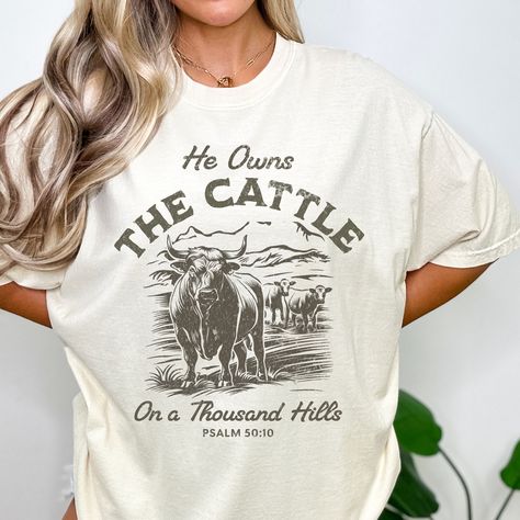 Embrace your faith with our boho western Christian shirt. This western cattle shirt is perfect for any homestead Christian, featuring cattle in front of a mountain landscape and the phrase "He Owns The Cattle On A Thousand Hills" from Psalm 50:10. It's an ideal tee for cow lovers and a great gift for those who cherish their Christian country roots. Our Western Christian design comes in our popular Comfort Colors t-shirt style and is printed for you from the highest quality materials possible.  C He Owns The Cattle On A Thousand Hills, Western Christian Shirts, Farm Tshirt Ideas, Western Tshirt Designs, Cattle On A Thousand Hills, Western Shirts For Women, Cow Shirts, Christian Country, Psalm 50