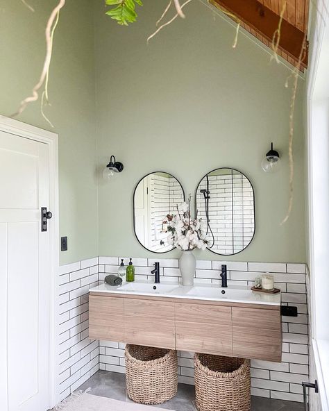 This corner bathroom draws attention to its sage green half walls and high vaulted ceiling with wood paneling. The bottom half of the walls are filled with white subway tiles. Accessorize the space with woven baskets that enhance the neutral tones of the cabinets. Neutral Bathroom Ideas, Luxurious Bathtubs, Brown Towel, Corner Bathroom, Beige Cabinets, Black Floor Tiles, Neutral Bathroom, Half Walls, White Subway Tiles