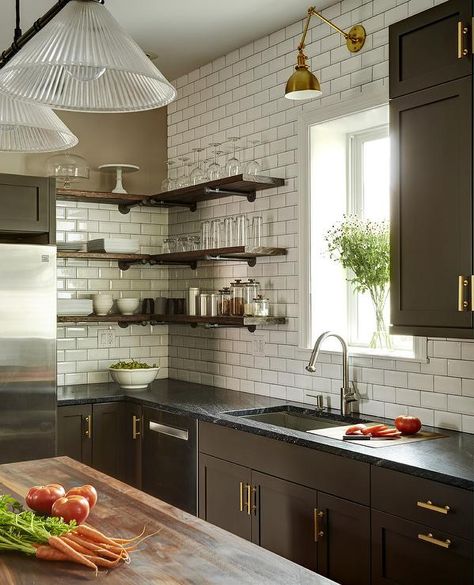 Gorgeous brown kitchen is fitted with L-shaped wood shelves stacked against white beveled subway tiles beside a window lit by a brass swing arm sconce mounted above a stainless steel sink with a polished nickel gooseneck faucet. Dark Brown Kitchen Cabinets, Wooden Kitchen Furniture, Dark Brown Kitchen, Kitchen Cabinets And Backsplash, Espresso Kitchen Cabinets, Espresso Kitchen, Brown Kitchen Cabinets, Brown Kitchen, Brown Kitchens