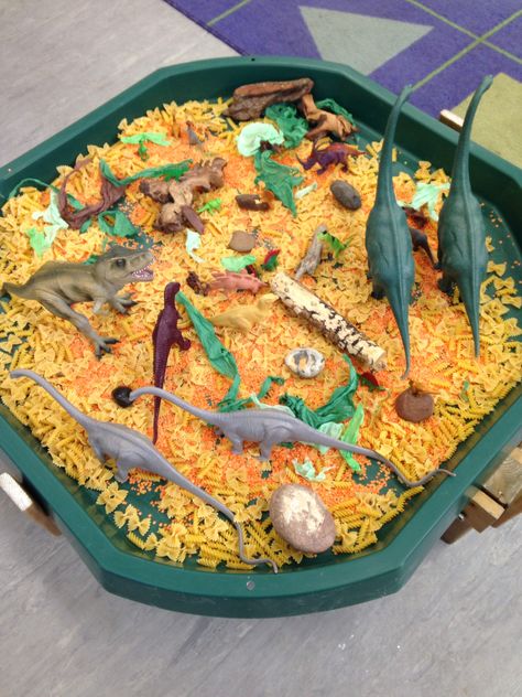 Tough tray dinosaur small world, I used pasta and lentils for texture and added natural resources e.g.  Wood, stones and green and brown shredded tissue paper. Dinosaur Tough Tray, Dinosaur Tough Tray Ideas, Pasta Tuff Tray Ideas, Dinosaur Tuff Tray Ideas, Dinosaur Tuff Tray, Dinosaurs Eyfs, Dinosaur Small World, Tuff Tray Ideas Toddlers, Dinosaur Theme Preschool