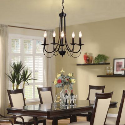 This 5-light chandelier features a classic empire silhouette with dashing curves and a streamlined design. Crafted entirely from metal with a sleek black finish, the arms go from the very top all the way down and curve back to the candlestick holders. On top of each one is a single 40W max bulb, sold separately, to cast a dimmable glow throughout your living room or dining area. We recommend getting flame-style bulbs to round out the modern farmhouse vibe. This chandelier hangs with the help of Traditional Black Chandelier, Modern Traditional Chandelier Dining Rooms, Farmhouse Light Fixtures Dining Areas, Dining Table Light Fixtures, Farmhouse Dining Room Light Fixtures, Minimalist Rooms, Modern Black Chandeliers, Candle Ceiling, Black Farmhouse Chandelier