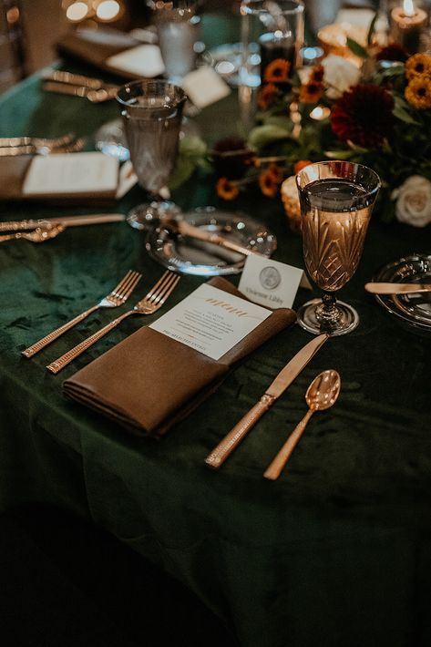 Round tables with dark green velvet and brown napkins with copper flatware make up this moody fall wedding reception table. Black Tablecloth With Green Runner, Wedding Brown And Green, Wedding Decor Forest Green, Copper Green Black Wedding, Green Gold And Brown Wedding, Dark Green Table Runner Wedding, Emerald Wedding Colors Decor, Copper And Forest Green Wedding, Brown And Green Wedding Colors