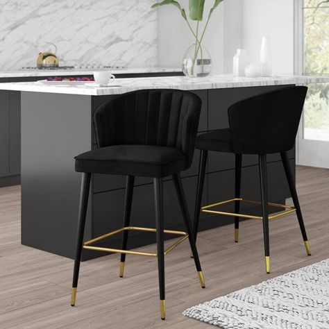 Pull up sleek, modern style to your kitchen island or counter with these bar stools. Four tapered and splayed solid wood legs in a black finish support the bar stools. Gold-finished capped feet and a square crossbar give the base a stylish two-toned look. Up top, the seat is upholstered in velvet and features a curved back with channel tufting and square seat with piped trim. These bar stools are sold in sets of two and require partial assembly. Velvet Bar Stools Kitchen Island, Bar Stools For Dark Kitchen Island, Black Island Stools Kitchen, Black Velvet Bar Stools, Bar Stools Black Kitchen Island, Black And Gold Counter Stools, Black Kitchen Island Chairs, Wayfair Bar Stools, Modern Black Bar Stools