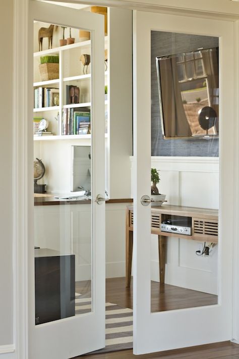 source: Belmont Design Group  Fabulous glass paned doors lead to a sunny office with hardwood floors layered with a gray and white striped area rug. The office features a built-in desk with bookshelves overhead. The lower walls are finished with batten and board trim and the upper walls papered in gray grasscloth. To the right of the glass doors stands a modern console with wall mounted flat screen. Internal Double Doors, Internal French Doors, Internal Glass Doors, Double Doors Interior, Double Glass Doors, Small Barn, Doors Interior Modern, Glass Doors Interior, French Doors Interior