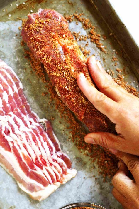 A hand rubbing the brown sugar mixture into a pork tenderloin. A stack of bacon is sitting next to it. Bacon Brown Sugar Pork Tenderloin, Pork Tenderloin Recipes In Oven Bbq, Cast Iron Pork Tenderloin, Bacon Wrapped Pork Tenderloin Oven, Pork Tenderloin Rub Recipes, Bbq Pork Tenderloin Recipes, Pork Loin With Bacon, Bacon Pork Tenderloin, Pork Tenderloin With Bacon